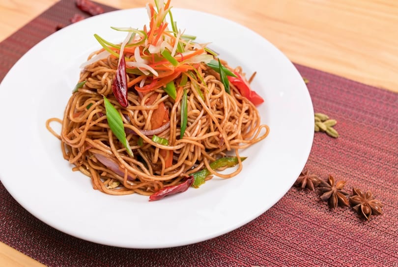 Noodles with colorful julienned vegetables and red chili peppers on a white plate.