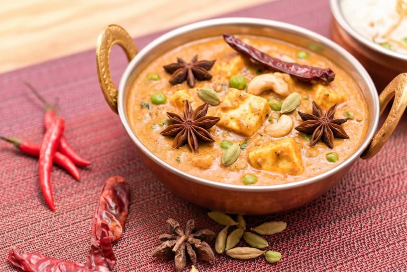 Indian paneer curry with peas, cashews, star anise, and dried chilies in a copper bowl.